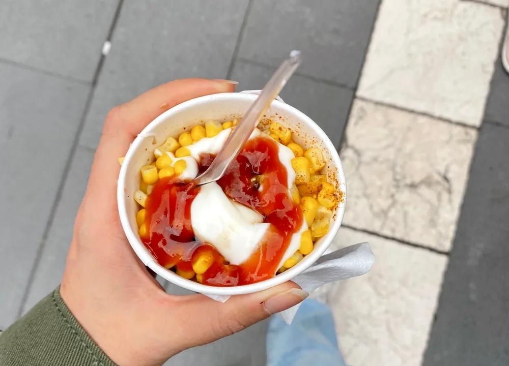 Close-up street corn cup topped with crema, cotija cheese, red chili seasoning and lime